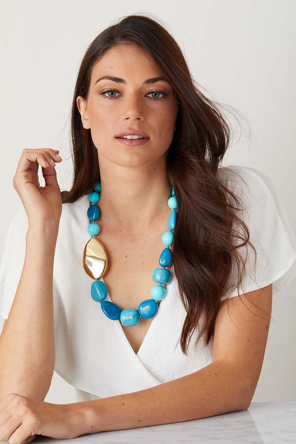 Blue turquoise gold statement necklace worn by a model in a white flowy top