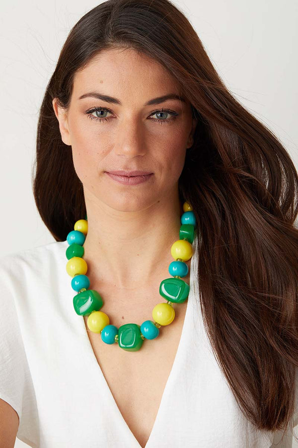Green yellow blue statement necklace worn by a model in a  white top