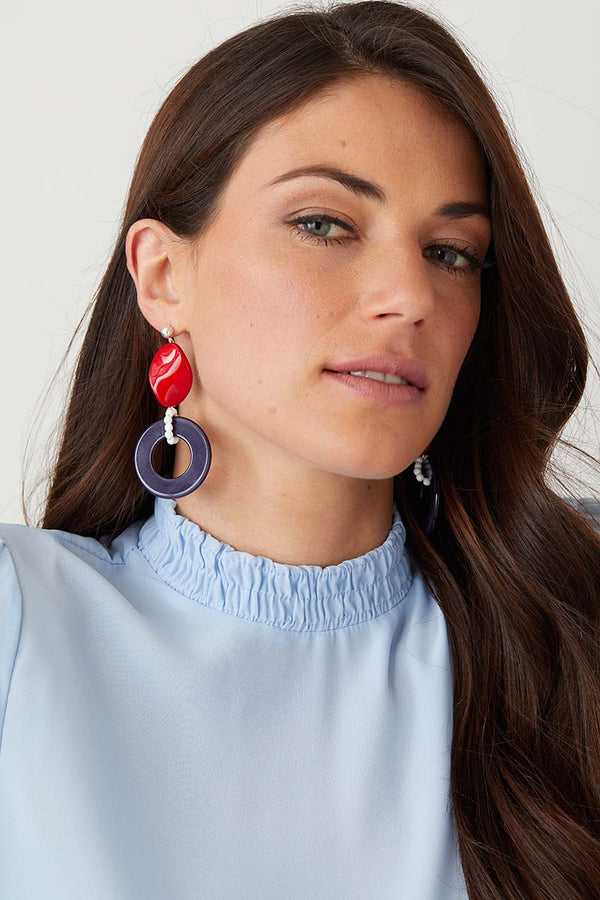 White red blue statement earrings worn by a model in a blue top