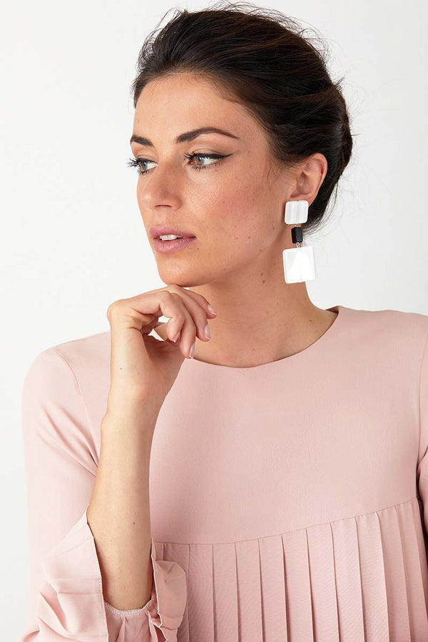 White black statement earrings worn by a model in a pink pleated dress