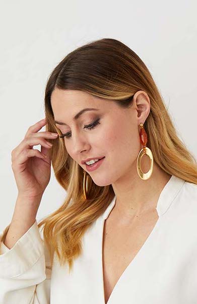 Gold amber drop statement earrings worn by a model in a  white top