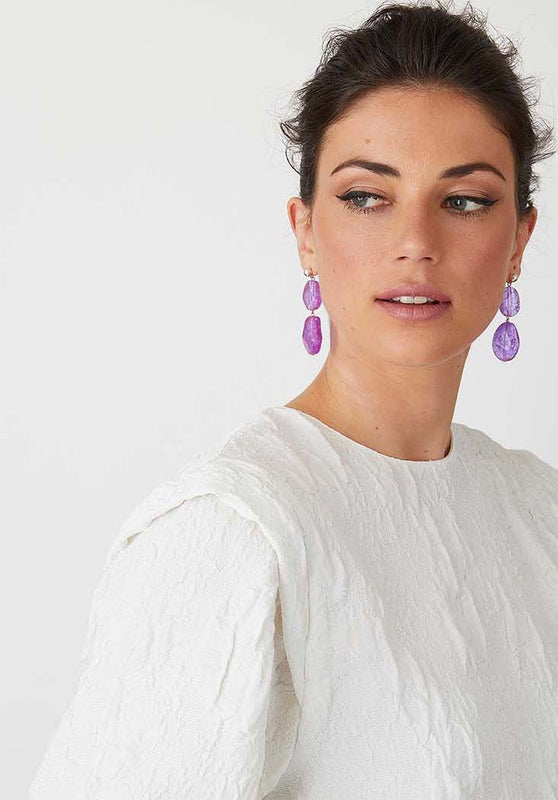 Purple resin statement earrings worn by a model in a white top