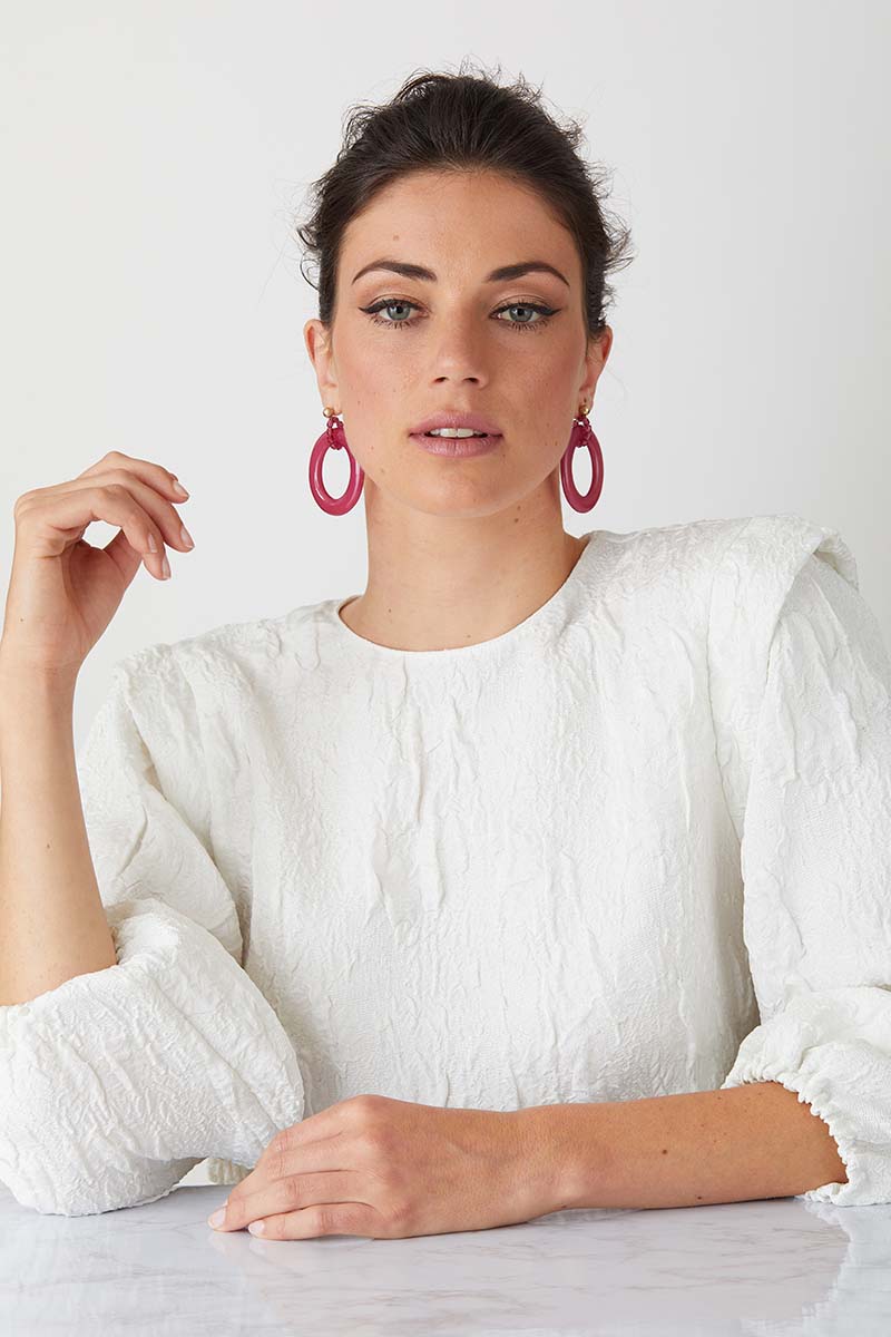 a pair of luxury italian pink statement earrings made of resin worn by a model in a white textured crew neck top