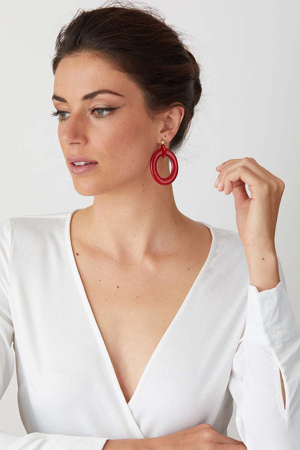 Red candy apple statement earrings worn by a model in a white low cut top