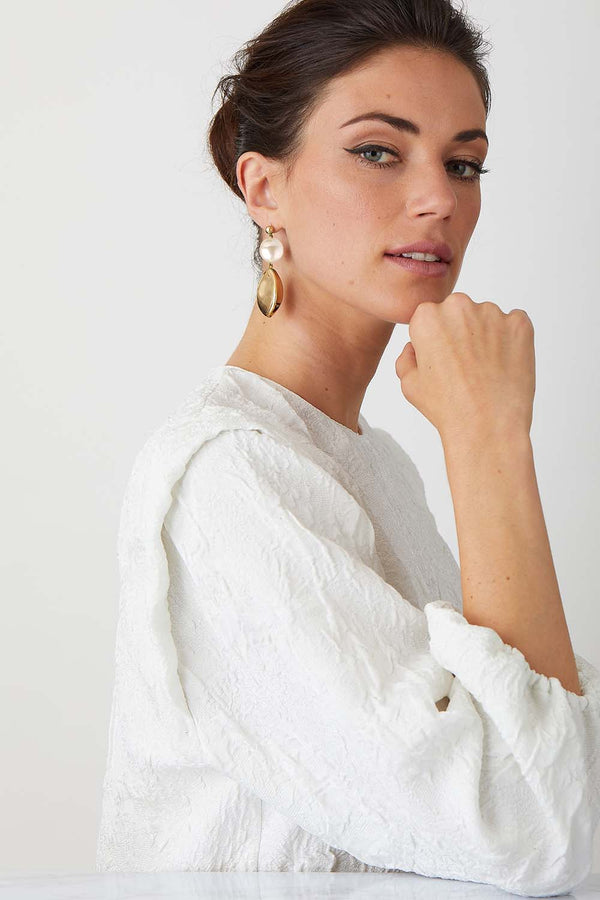 Orange gold statement earrings worn by a model in a high fashion white top