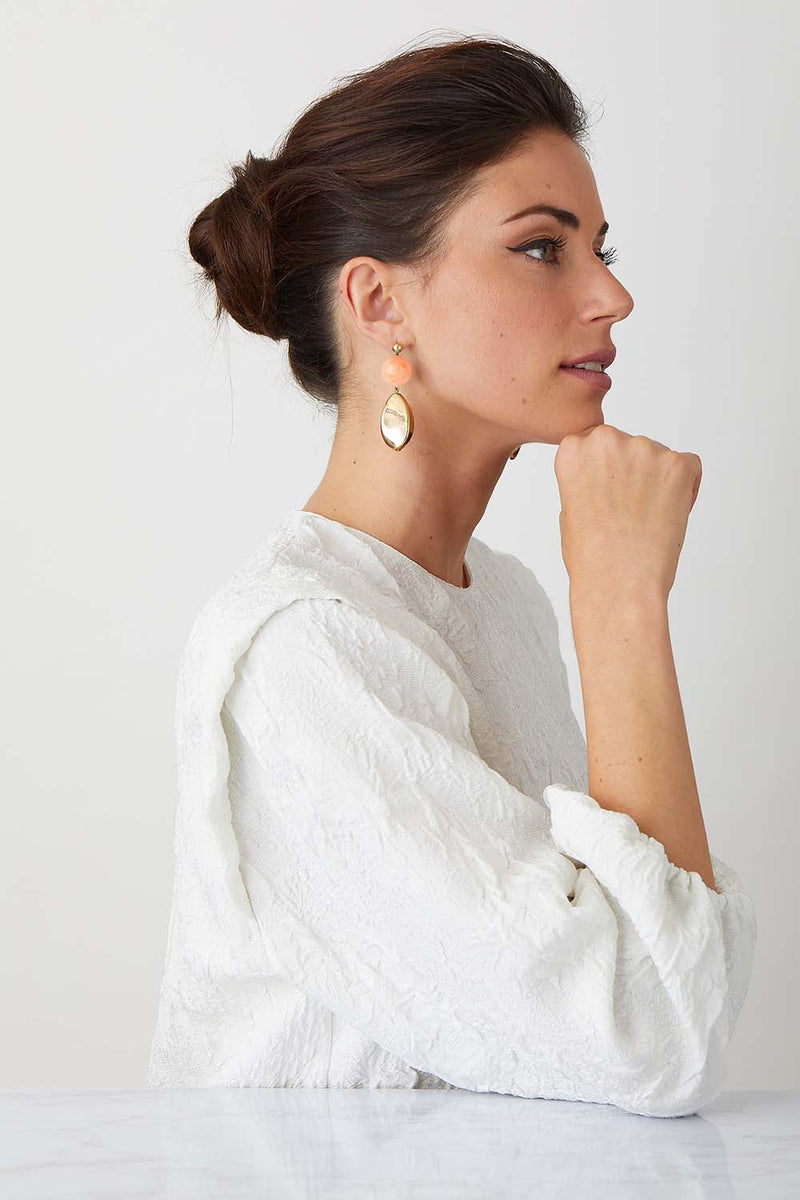 Pink burl gold statement earrings worn by a model in a white top