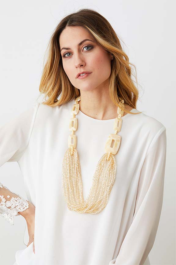 Ivory cream long crystal statement necklace worn by a model in a  white laced top