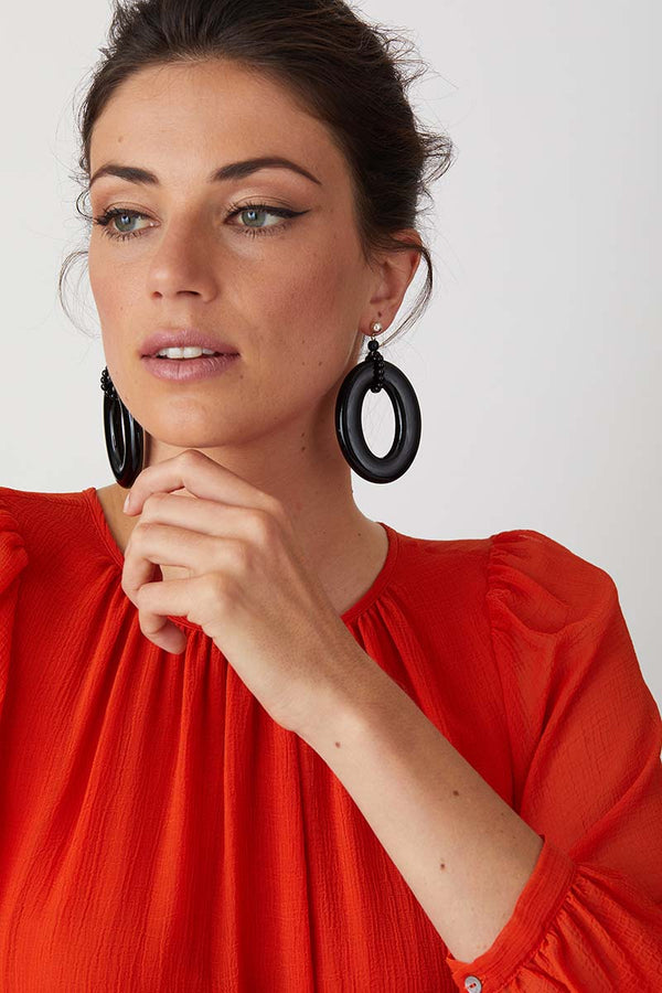 Black hoop statement earrings worn by a model in a flowy red dress