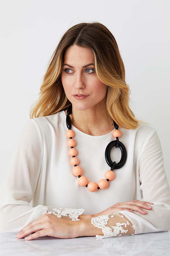 Pink black statement necklace worn by a model in a white laced top