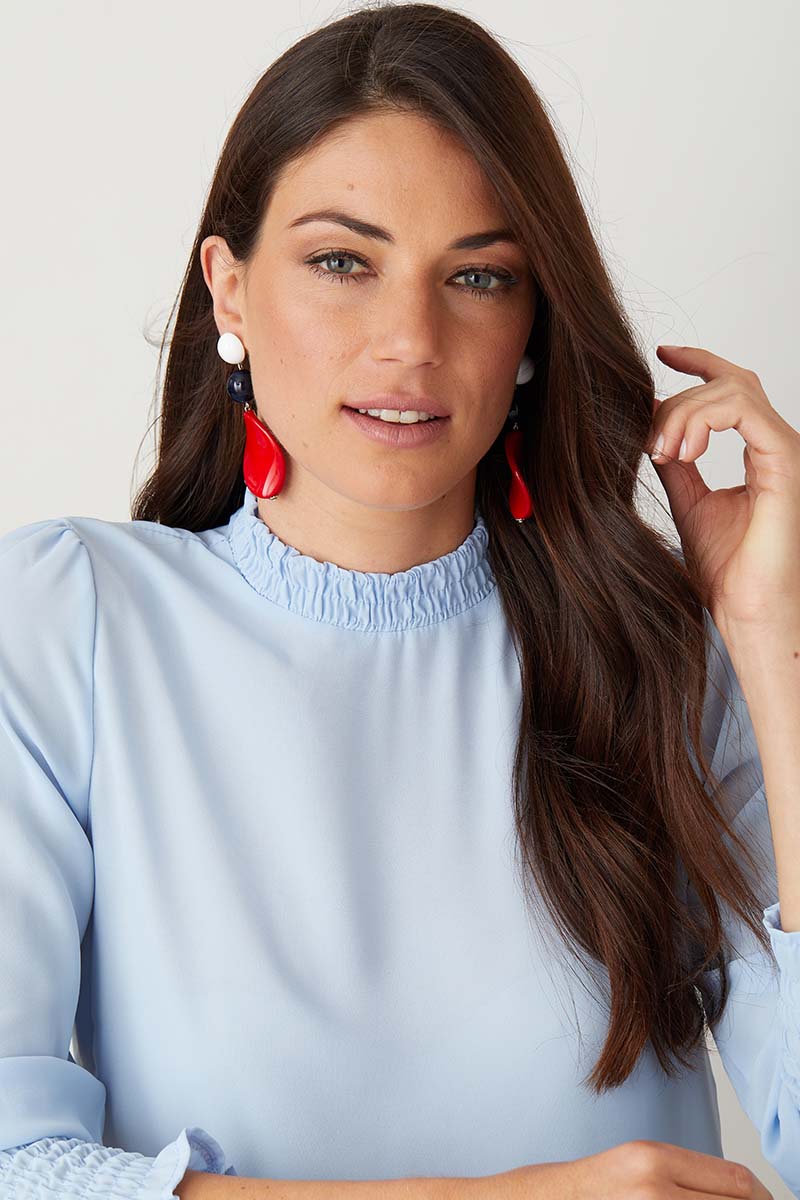 White red blue statement earrings worn by a model in a blue top