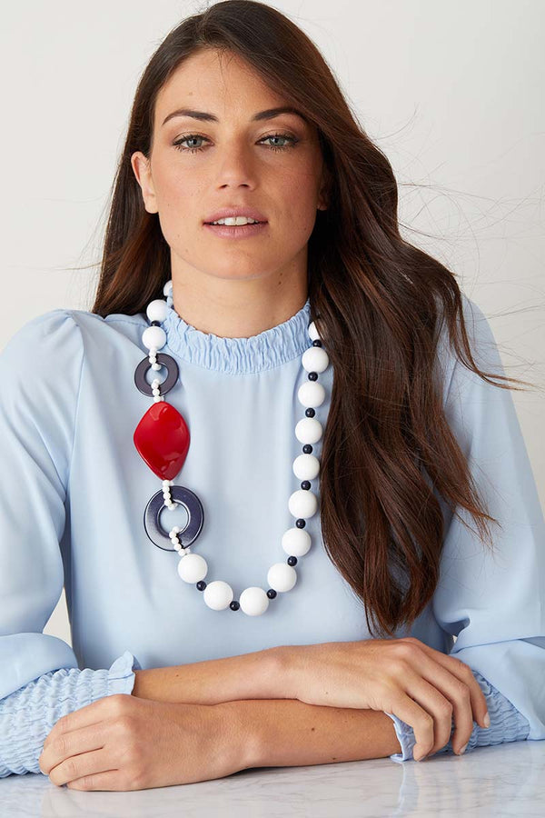 White red blue statement necklace worn by a model in a blue top
