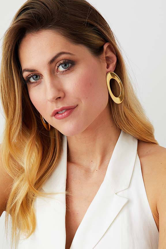 Gold hoop statement earrings worn by a model in a white summer dress