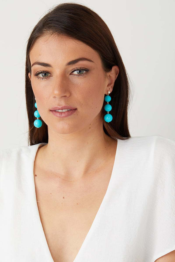 Light blue turquoise statement earrings worn by a girl in a white top