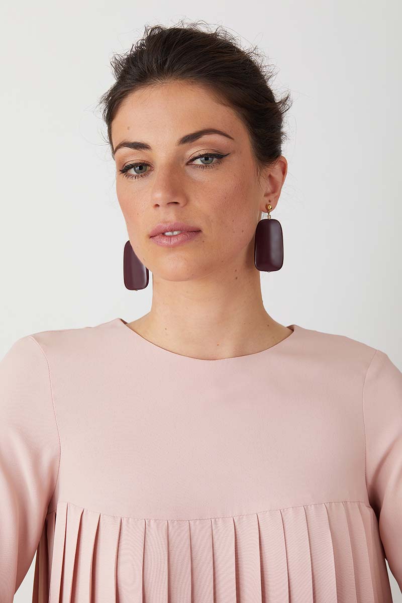 Burgandy statement earrings worn by a model in a pink pleated dress