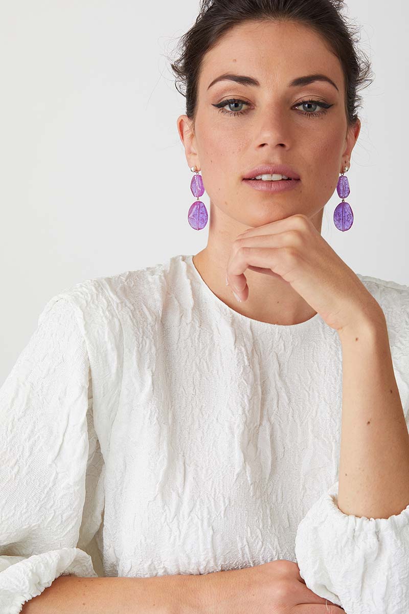 Purple statement earrings worn by a model in a white high fashion top